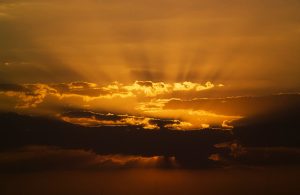 Sun setting behind clouds. The sky is deep orange.